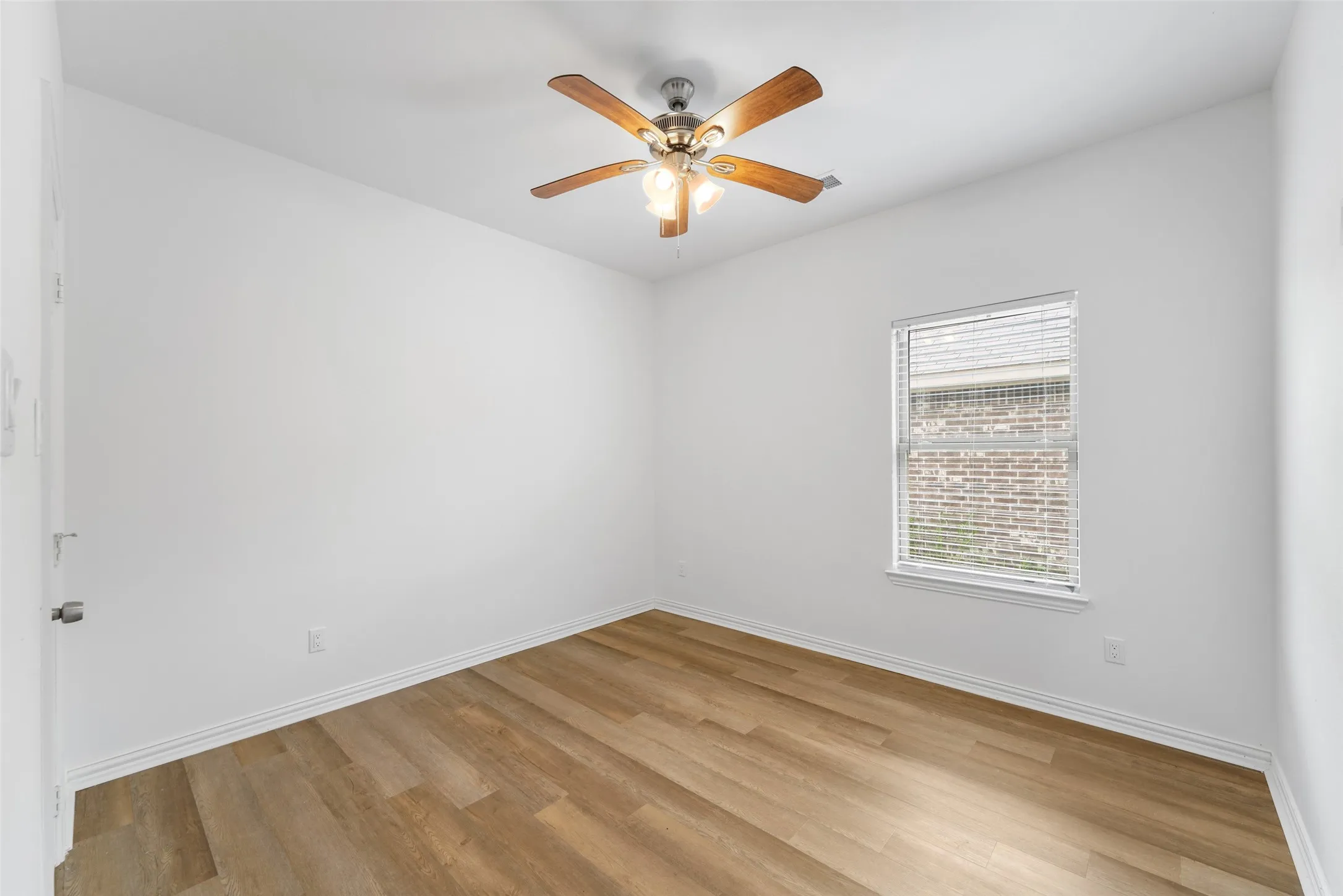Room featuring wood-finish flooring, white baseboards, a ceiling fan with integrated lighting, and a window with blinds
