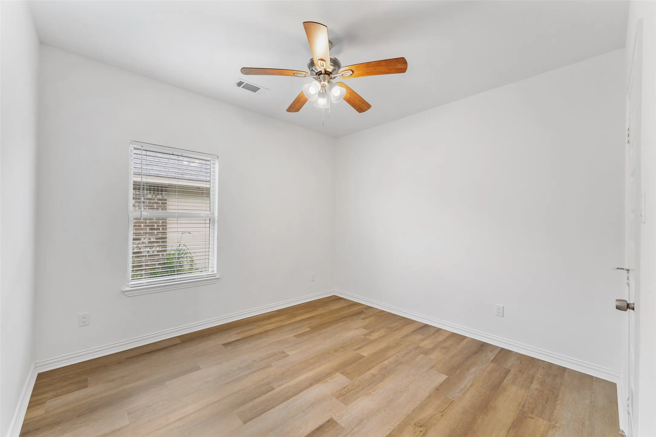 Room featuring wood-finish flooring, white baseboards, a white ceiling fan with integrated lighting, and a window with blinds