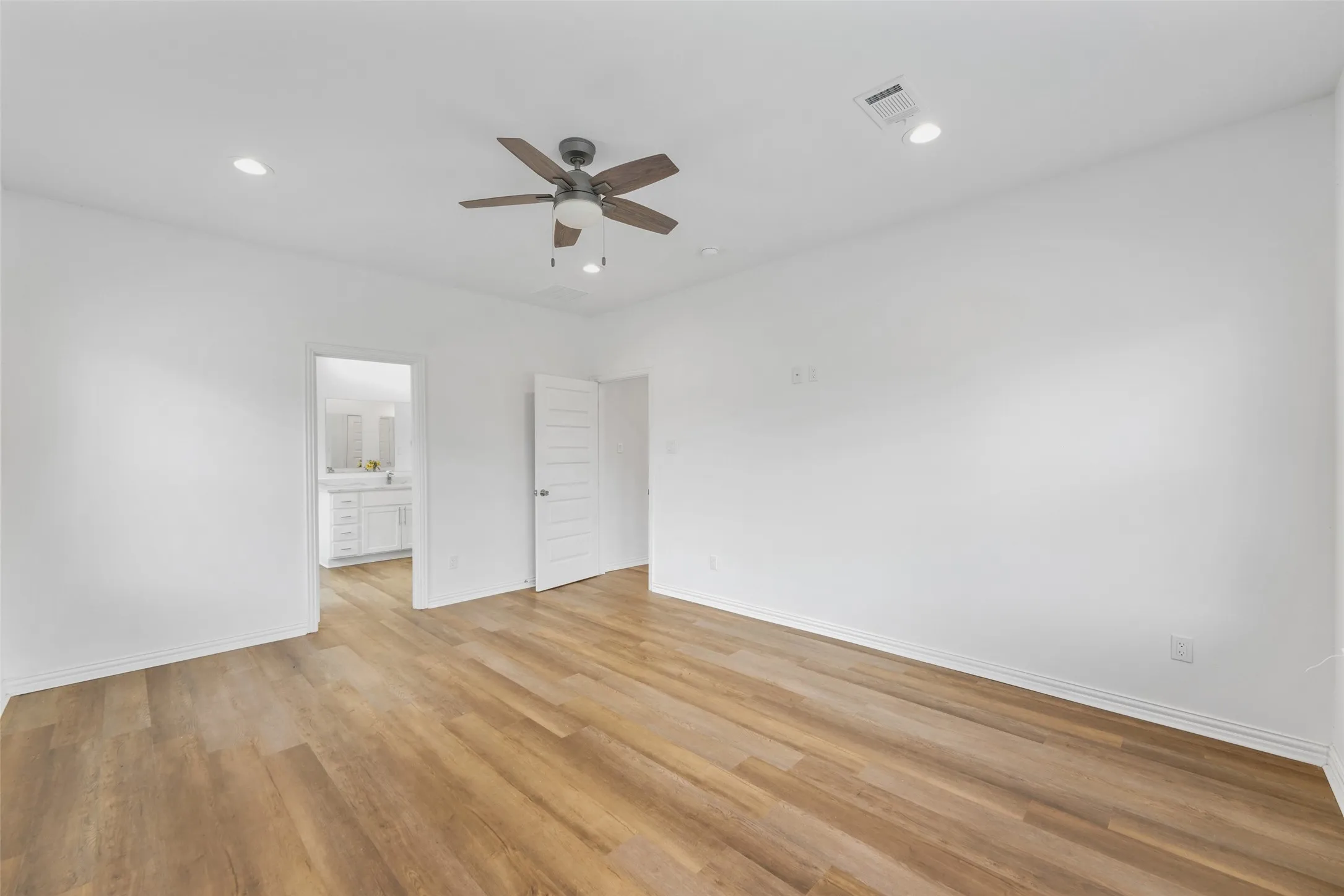 Spacious room featuring wood-finish flooring, white walls, and a ceiling fan with integrated lighting