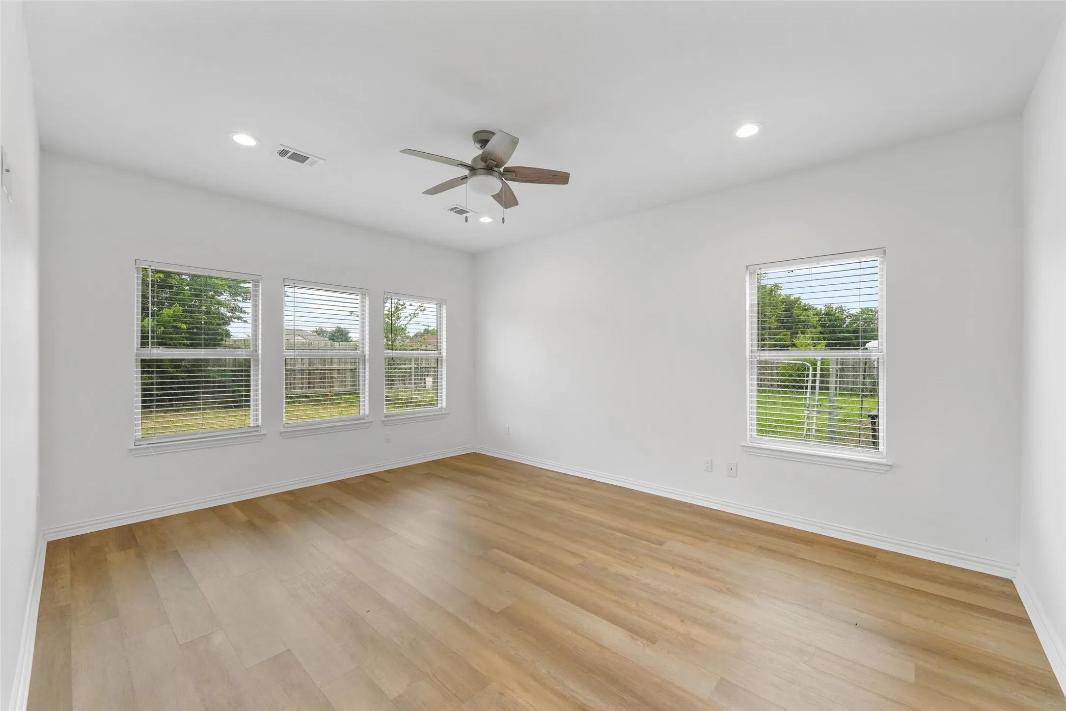 Bright interior space featuring wood-finish flooring, white walls, and multiple windows with blinds