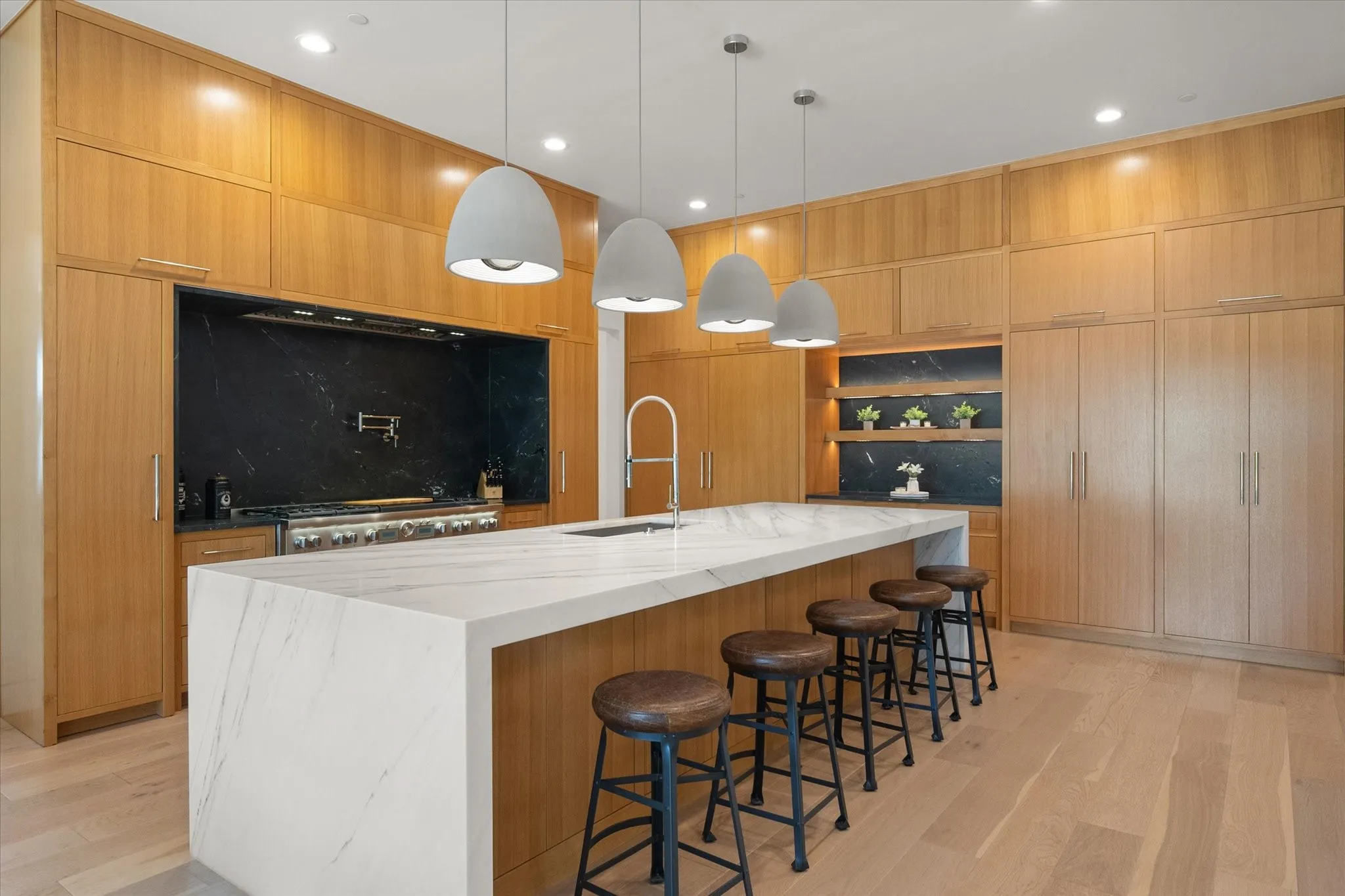 Gourmet Kitchen featuring a large waterfall island with a light countertop, a professional-grade Thermador range. Integrated wood cabinetry, a dark stone backsplash, recessed and pendant lighting. Full Thermador appliance package.