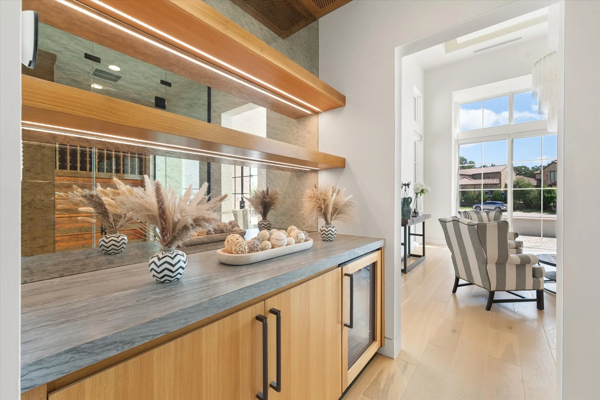 Custom built-in bar with wood-finish cabinetry, stone countertop, integrated beverage refrigerator, and mirrored backsplash with accent lighting.
