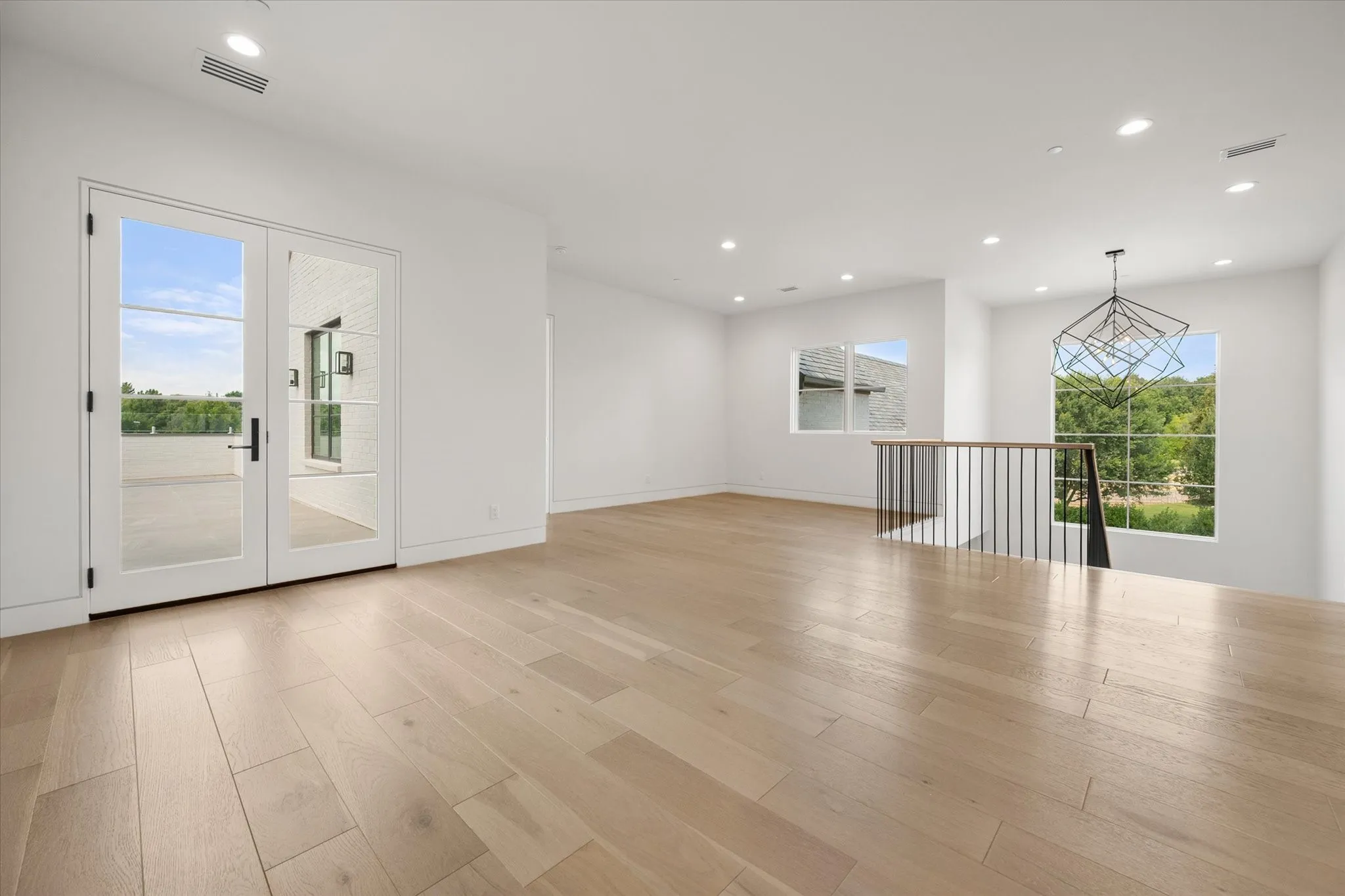 Upstairs versatile entertainment game room or secondary living area with access to an upstairs balcony. Features include the light wood-finish floors, recessed lighting, and a modern geometric pendant light fixture.