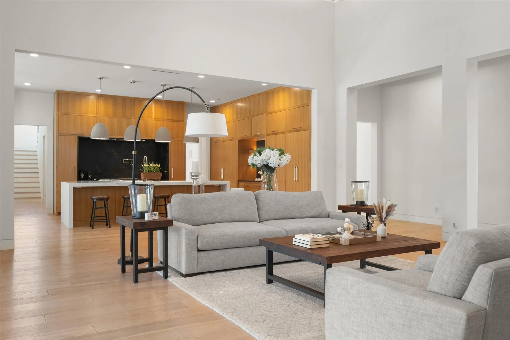Open-concept living and kithen space featuring wood-finish flooring, a kitchen island with seating, a dark backsplash, and light wood cabinetry in the kitchen.
