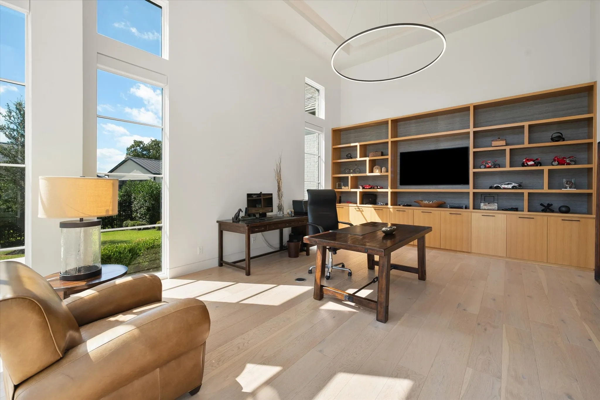 Vaulted ceiling in the office area featuring large-pane windows, light wood-finish flooring, and a full-wall built-in shelving unit with integrated cabinetry
