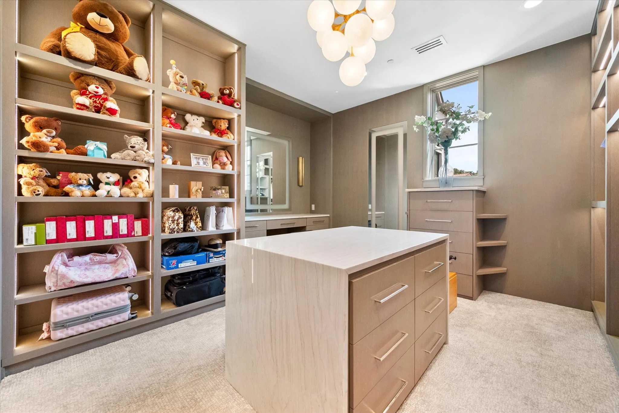 Custom closet space featuring a central island with integrated drawers, extensive built-in shelving with recessed lighting, a window providing natural light, and plush carpeting