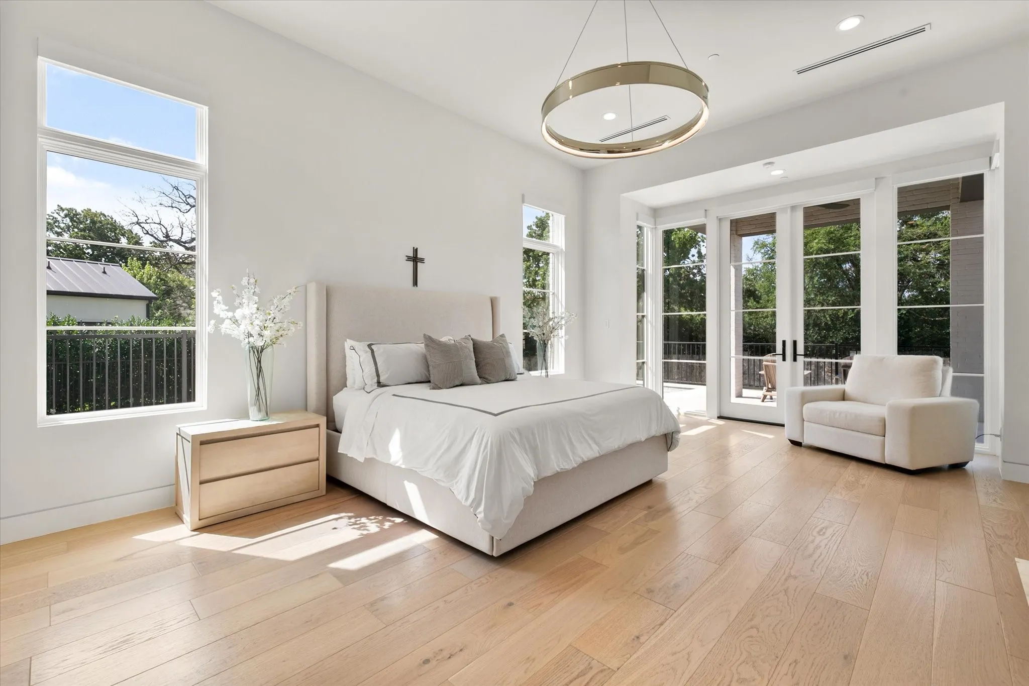 Bright natural light primary bedroom featuring wood finish flooring, modern circular chandelier, recessed lighting, and expansive glass doors opening to an exterior backyard