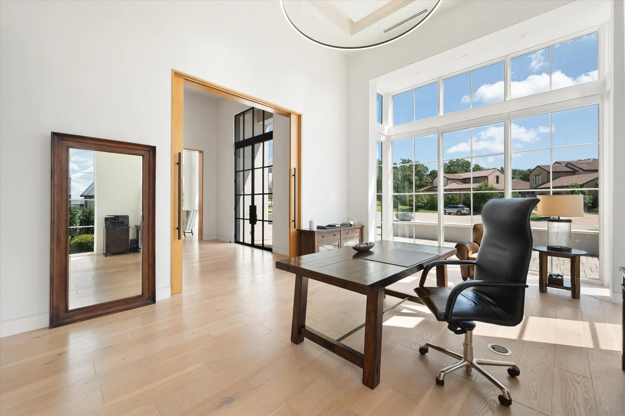 Double-height office area featuring light wood-finish flooring, a contemporary ceiling light fixture, and a wall of windows with view.