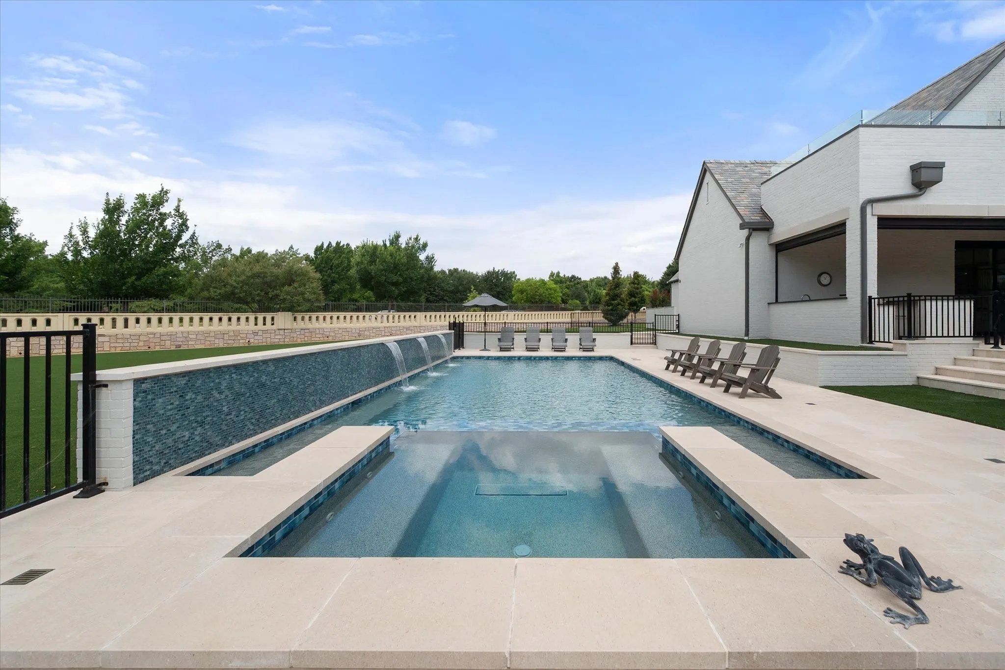 Outdoor area featuring a rectangular pool with integrated spa, a tiled waterfall wall, and light-toned hardscaping.