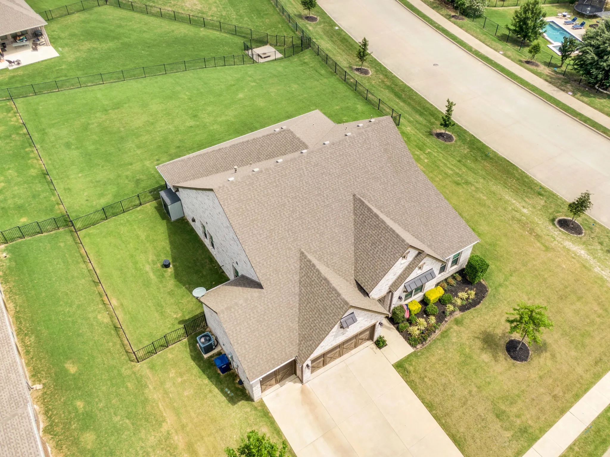 Stone and siding exterior with a multi-level shingle roof, featuring a two-car garage, a concrete driveway, and a fenced backyard with mature landscaping