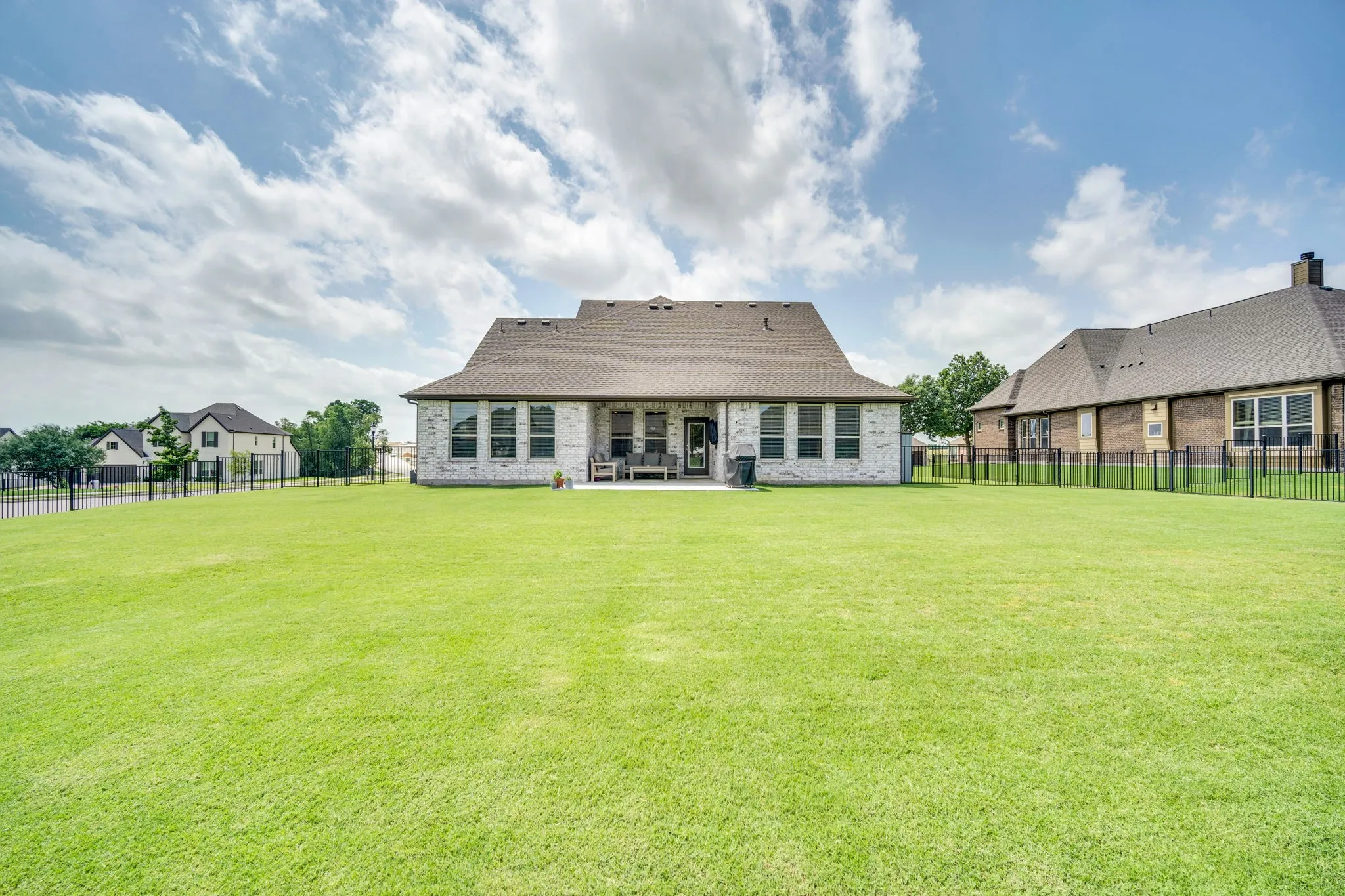 Expansive backyard featuring a large green lawn, a covered patio, brick exterior, and a dark shingle roof