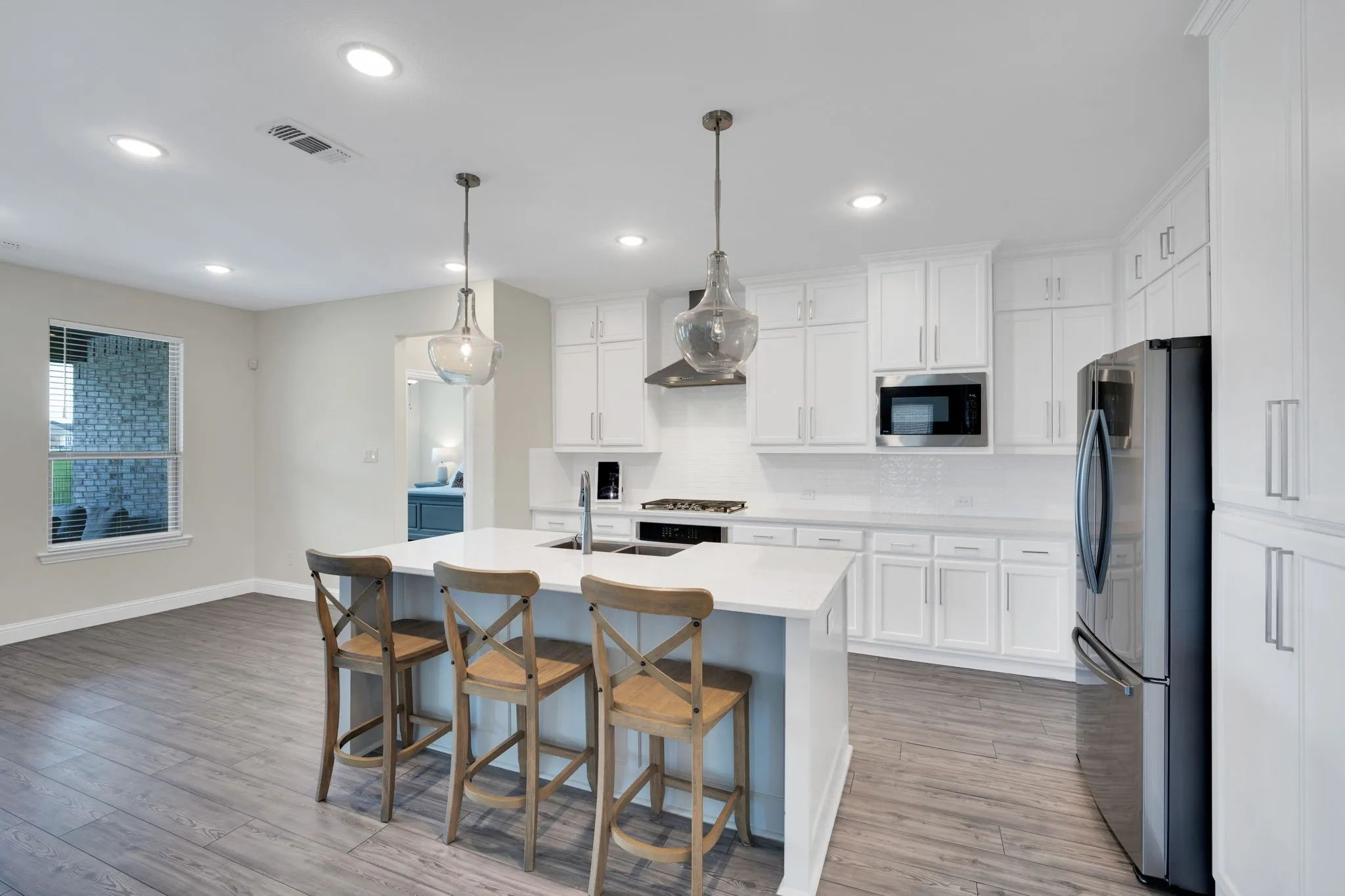 Kitchen featuring a large island with counter seating, white shaker cabinetry, stainless steel appliances, and wood-finish flooring