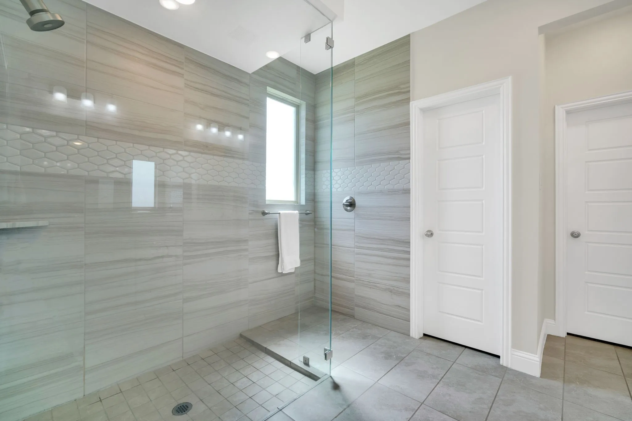 Walk-in shower featuring large format tile, a decorative honeycomb tile band, a fixed shower head, and a glass enclosure