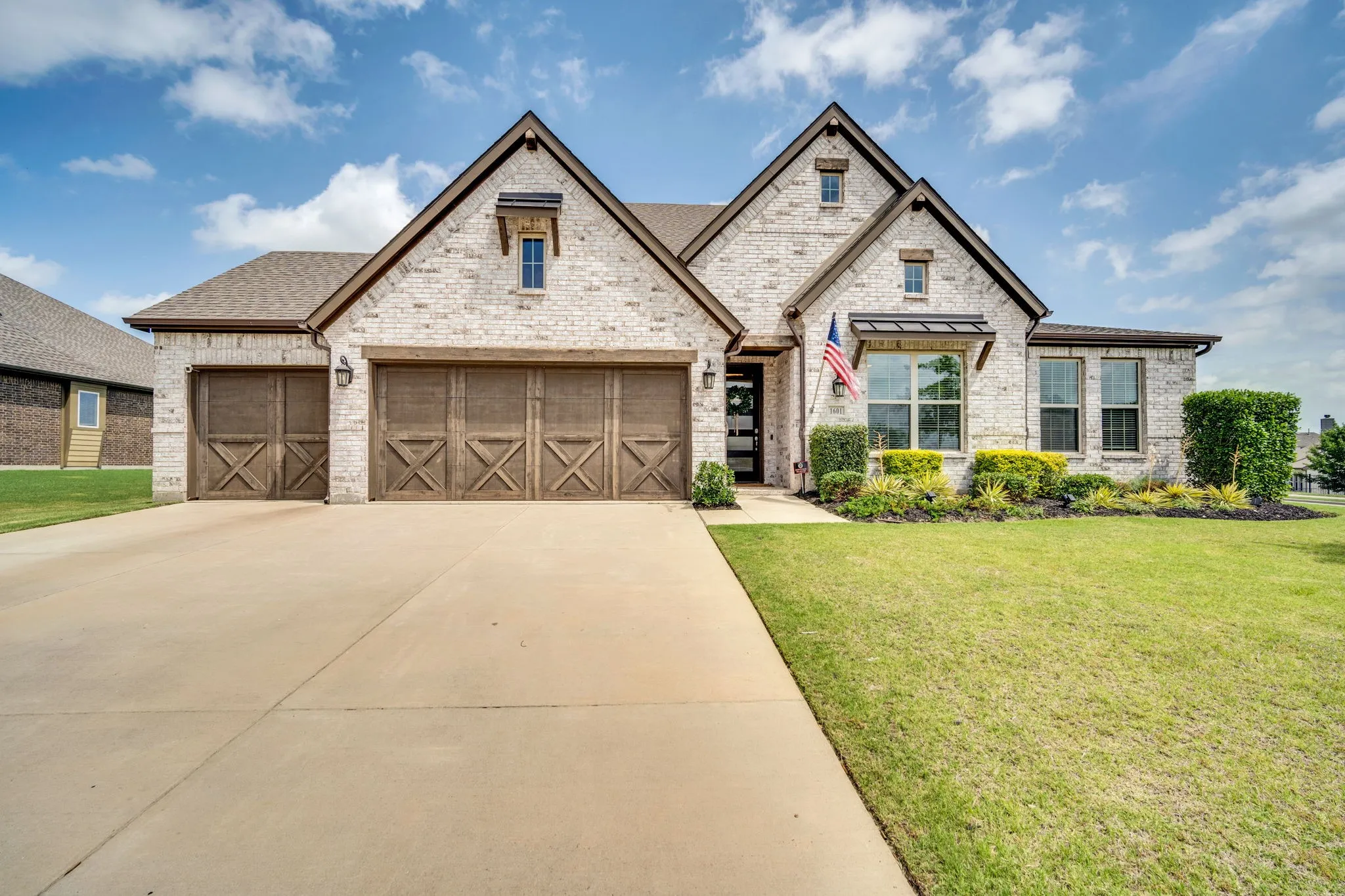 Brick exterior featuring multiple gables, a three-car garage with wood-finish doors, and a concrete driveway