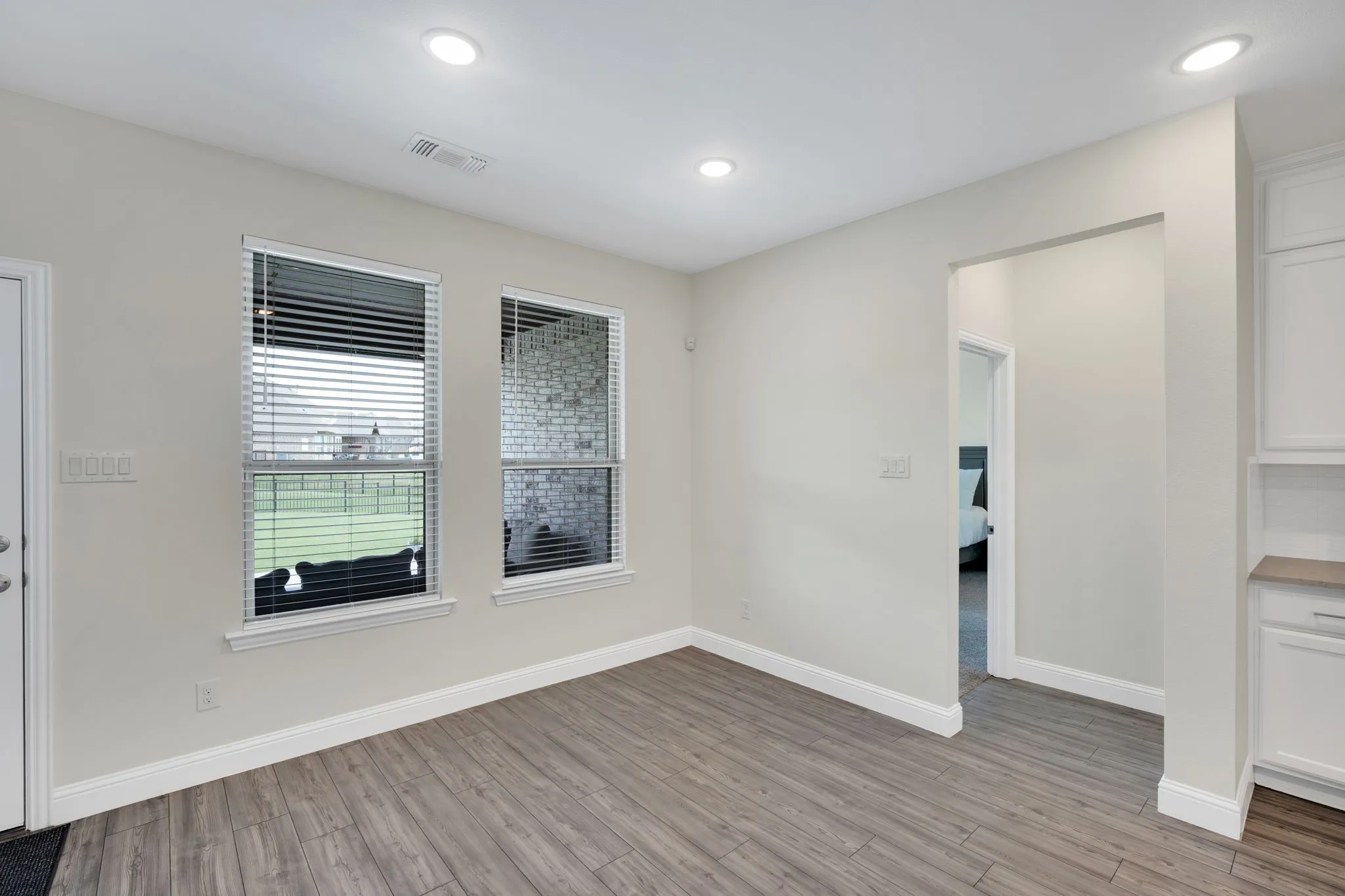 Spacious room featuring wood-finish flooring, recessed lighting, and two windows with horizontal blinds