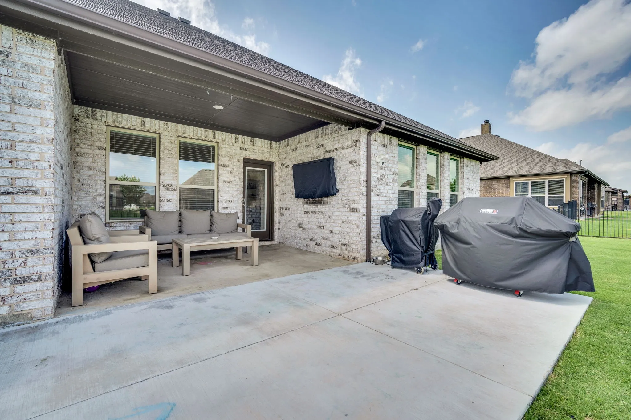 Covered concrete patio featuring a white brick exterior, recessed lighting, and a dark brown door frame