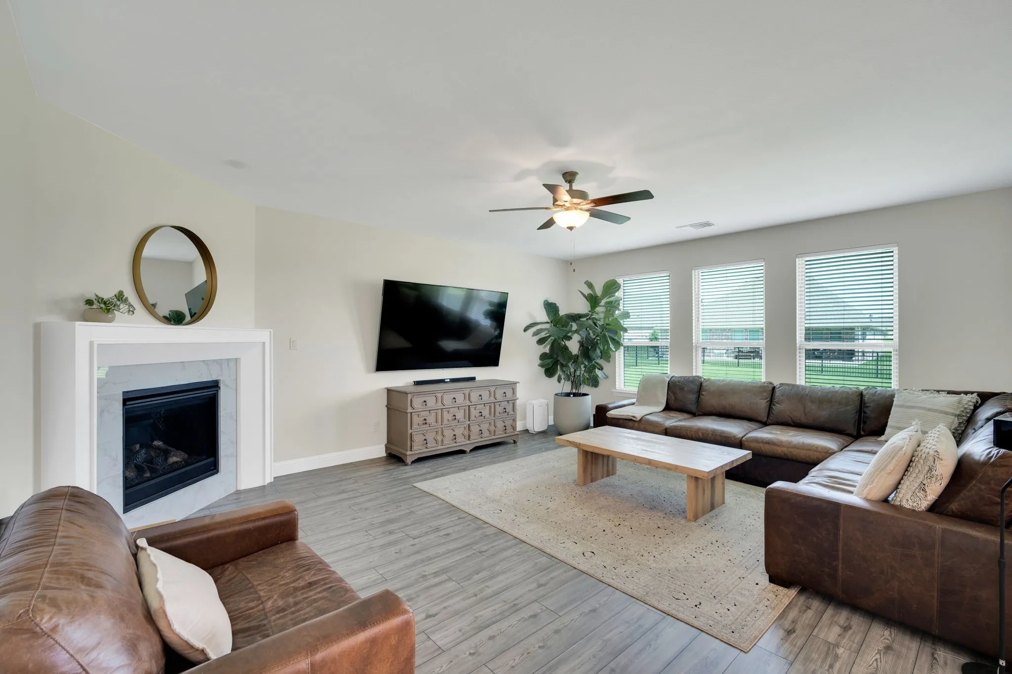 Spacious living area featuring wood-finish flooring, a fireplace with a white mantel and stone surround, and multiple windows with horizontal blinds