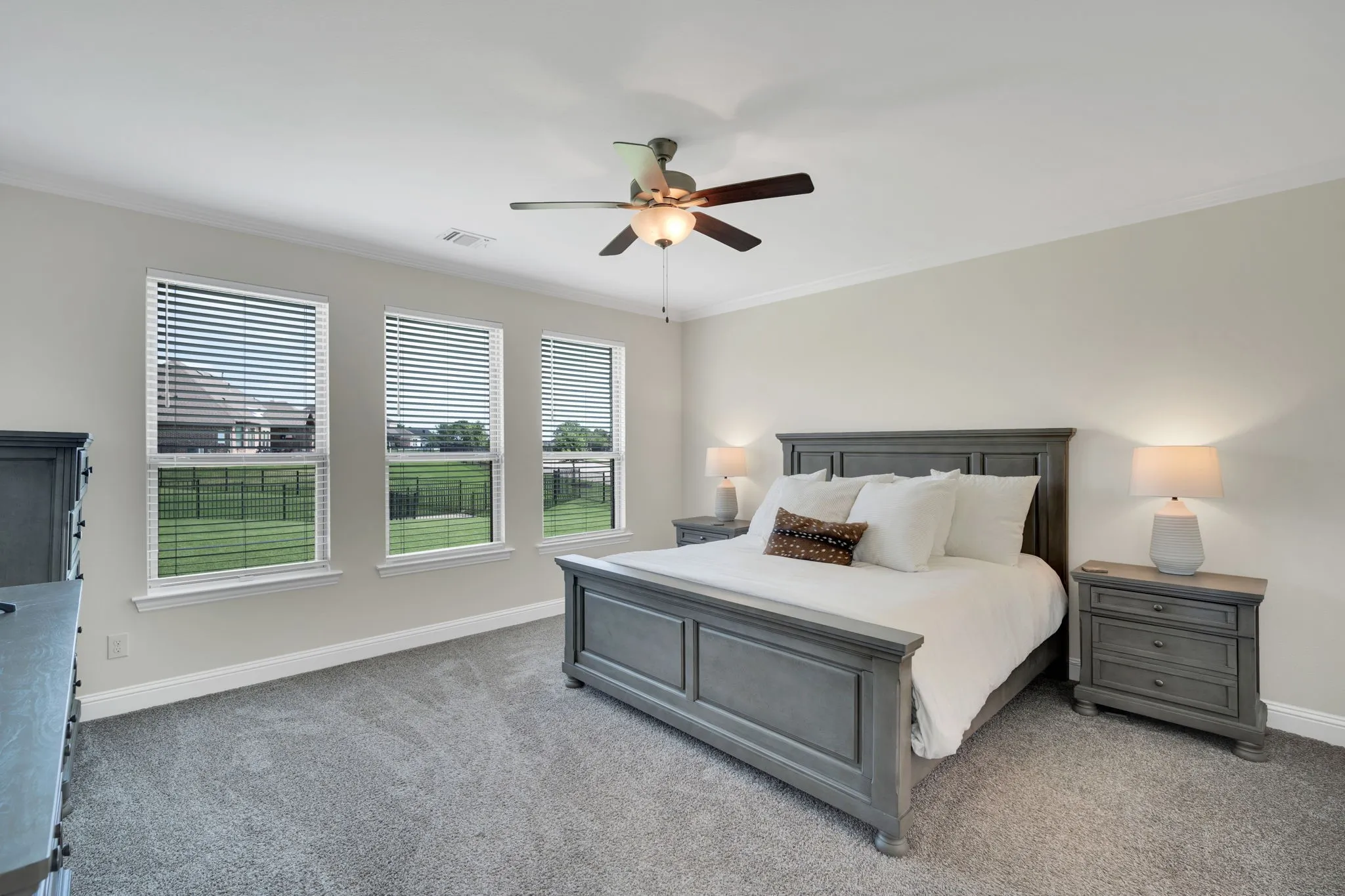 Expansive room featuring three large windows with horizontal blinds, plush carpeting, a ceiling fan with integrated lighting, crown molding, and baseboards