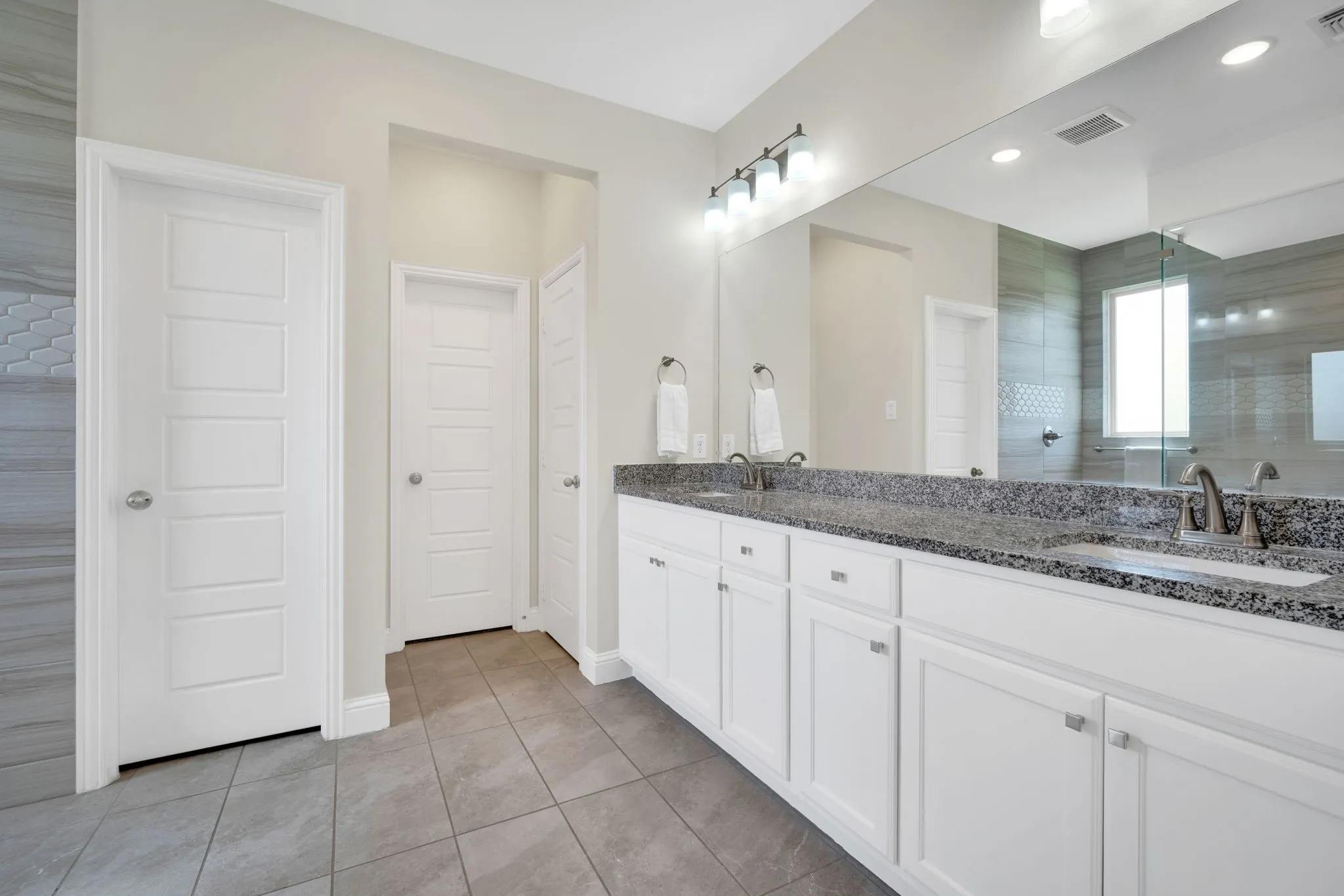 Spacious bathroom featuring a dual vanity with granite countertops and white cabinetry