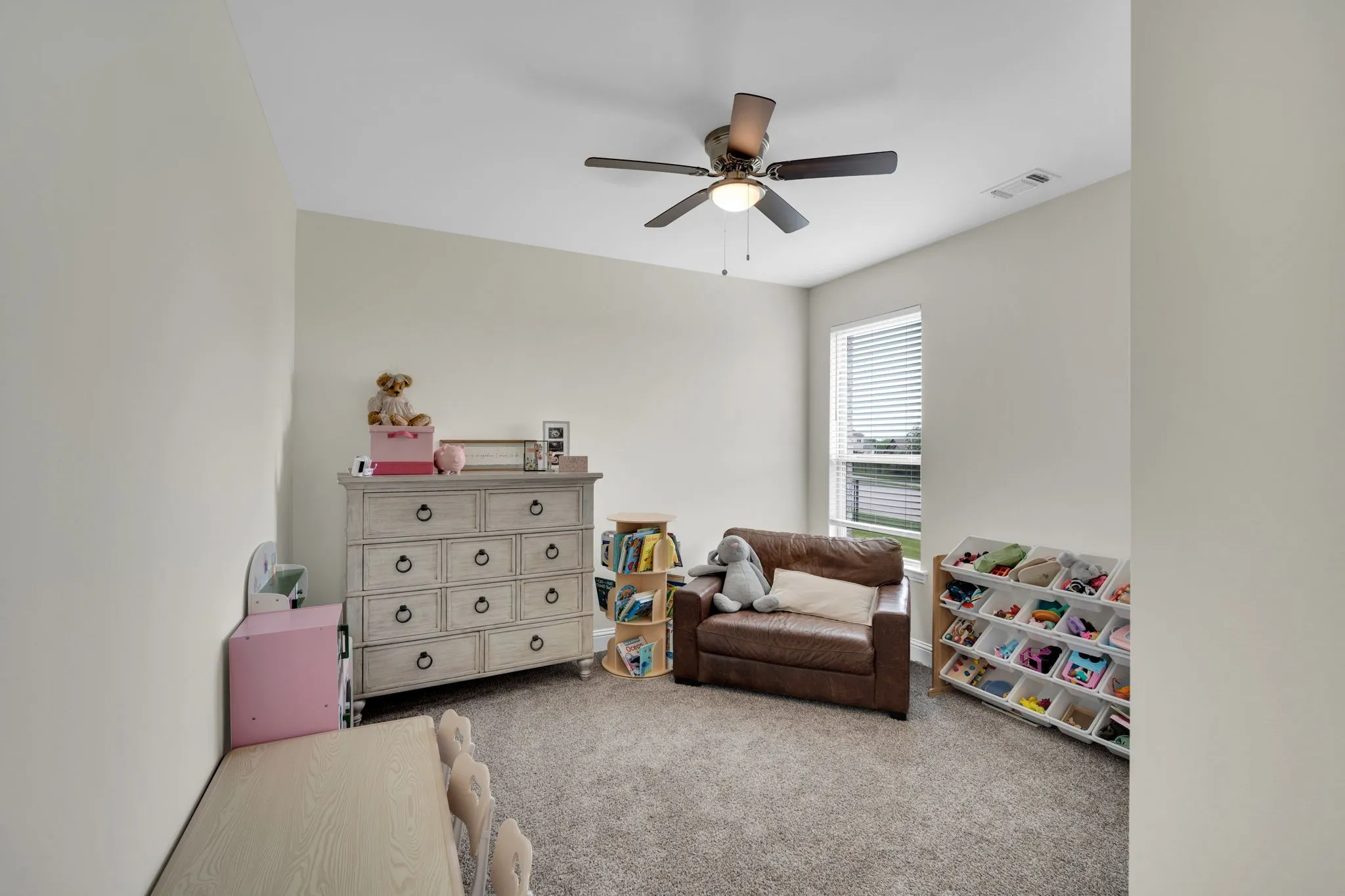 Neutral-toned room featuring a ceiling fan with integrated lighting, a single window with blinds, and soft carpet flooring