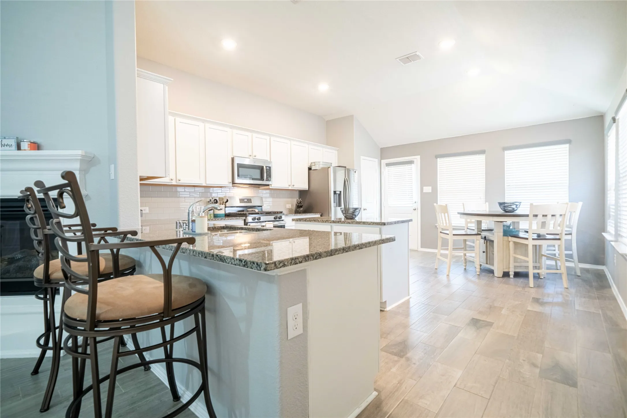 Kitchen featuring dark stone counters, white cabinetry, light hardwood / wood-style floors, appliances with stainless steel finishes, and lofted ceiling