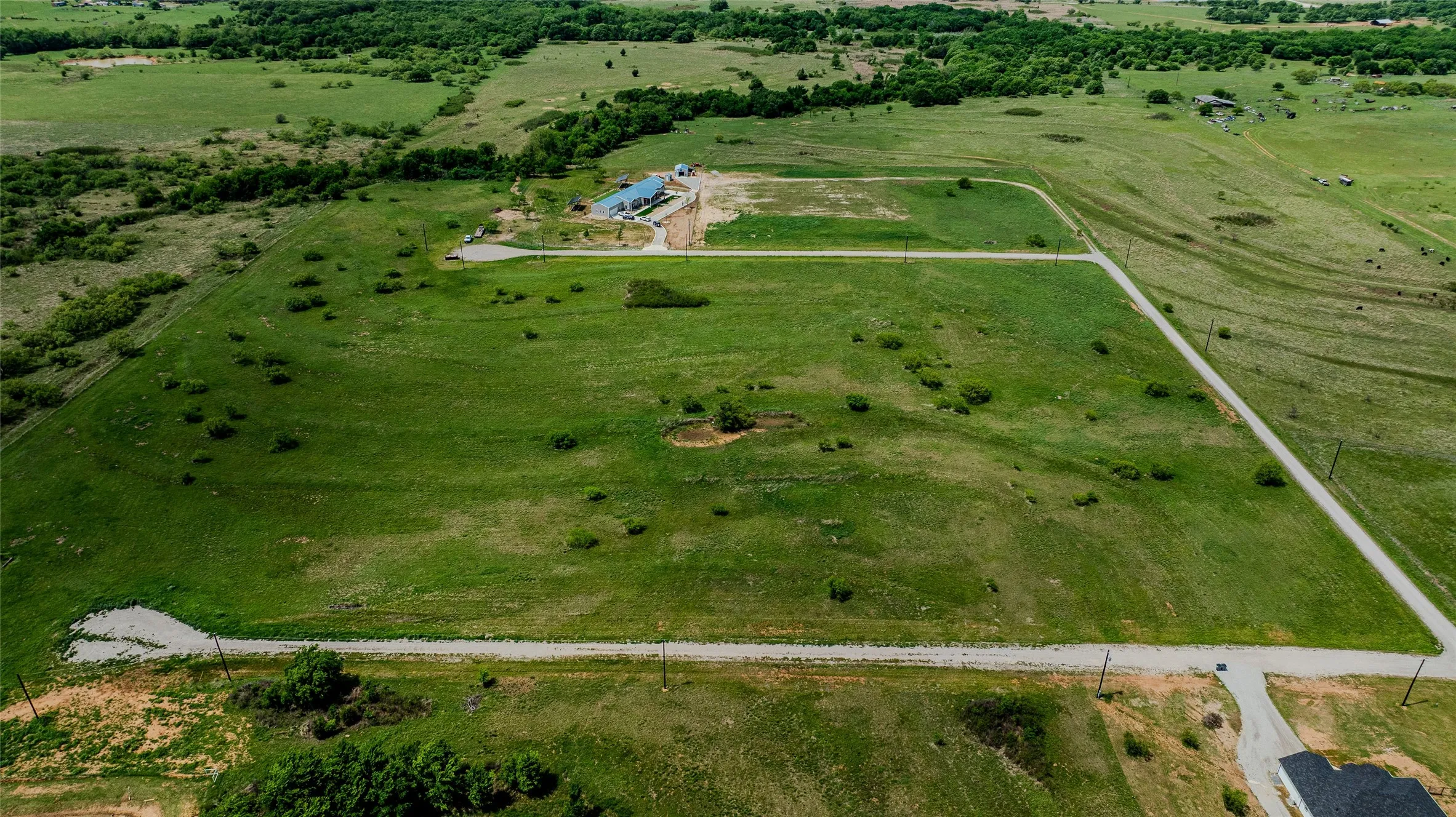 Expansive undeveloped land parcel featuring a central building under construction, established perimeter roads, and existing utility poles