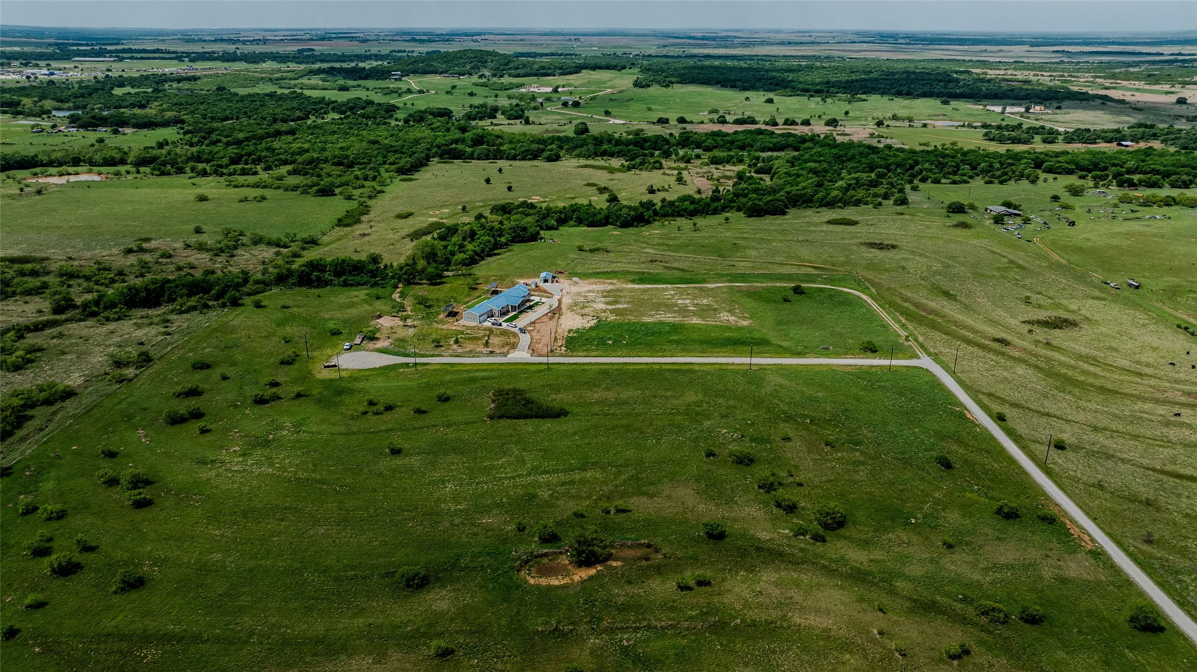 Expansive rural acreage featuring a newly constructed building, a private pond, and a paved access road