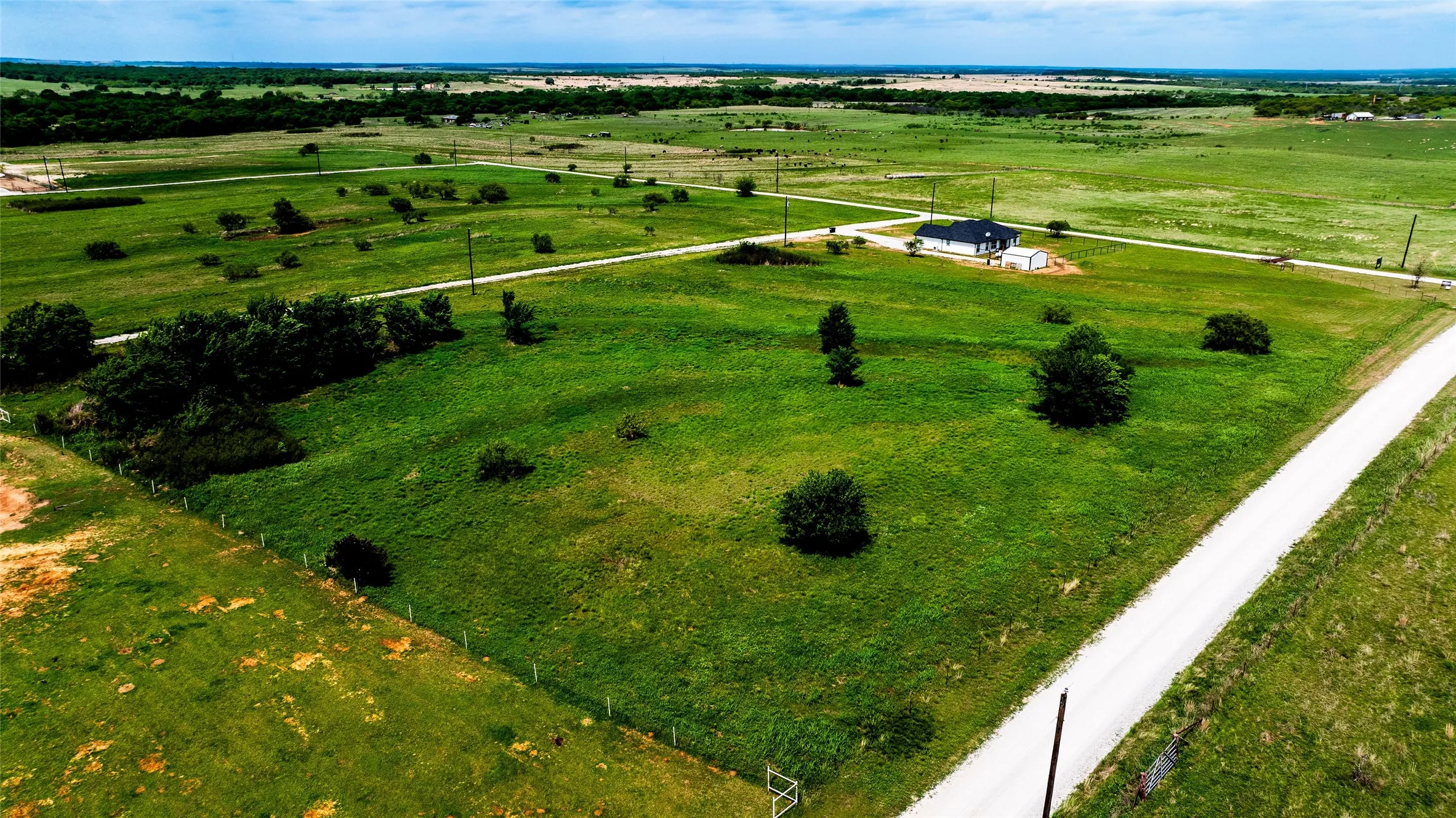 Expansive green landscape with a distant contemporary-style residence featuring a dark roof and light-colored siding