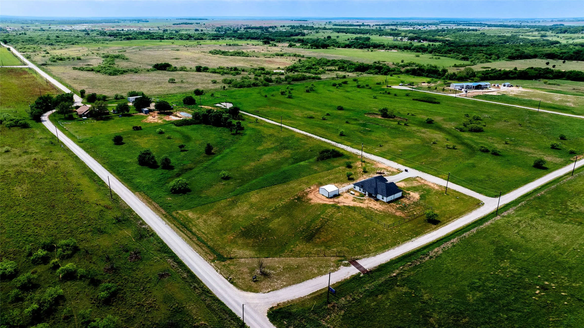 Expansive green landscape featuring an angular-roofed residence, a detached shed, and two intersecting roads