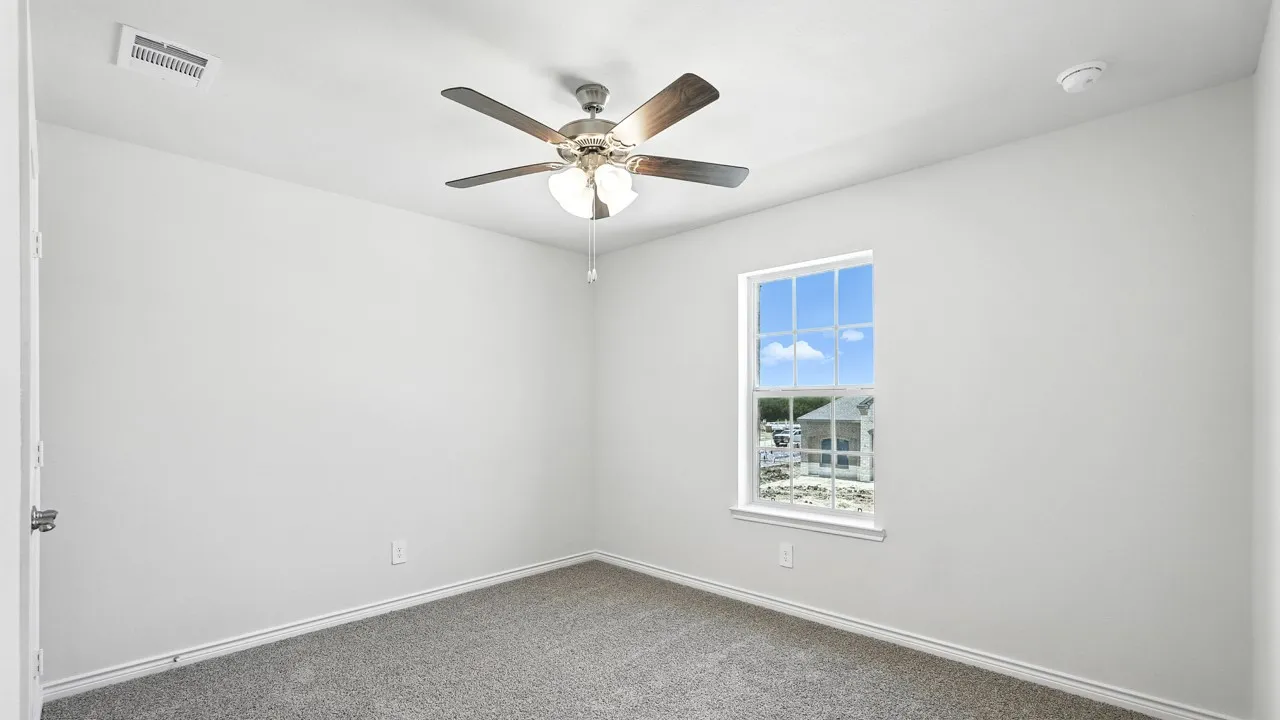 Neutral toned walls with a single window, ceiling fan with integrated lighting, and gray carpeted flooring