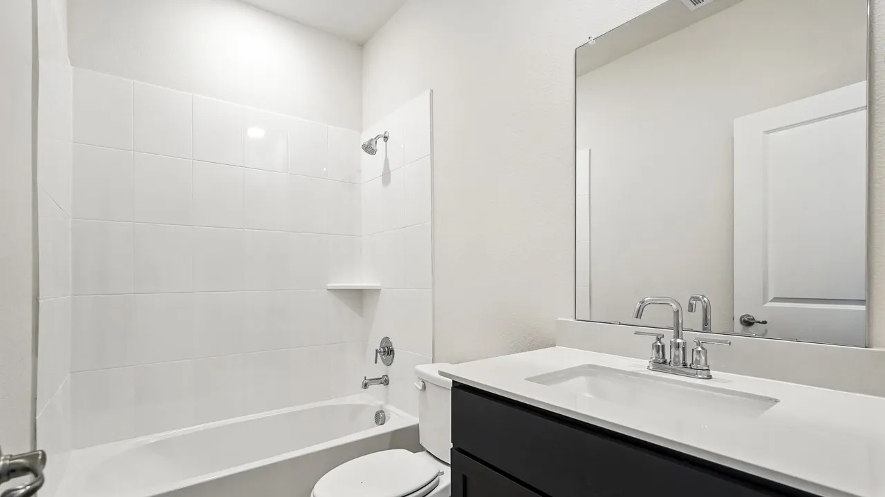 Bathroom featuring a white tile shower surround, a built-in shower shelf, a dark wood-finish vanity with an integrated sink, a light-toned countertop, and a large wall-mounted mirror
