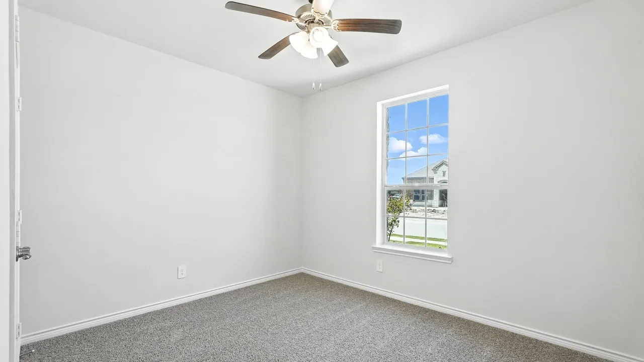 Room featuring a ceiling fan with light fixture, single window with grid pattern, neutral gray carpeting, white baseboards, and white painted walls