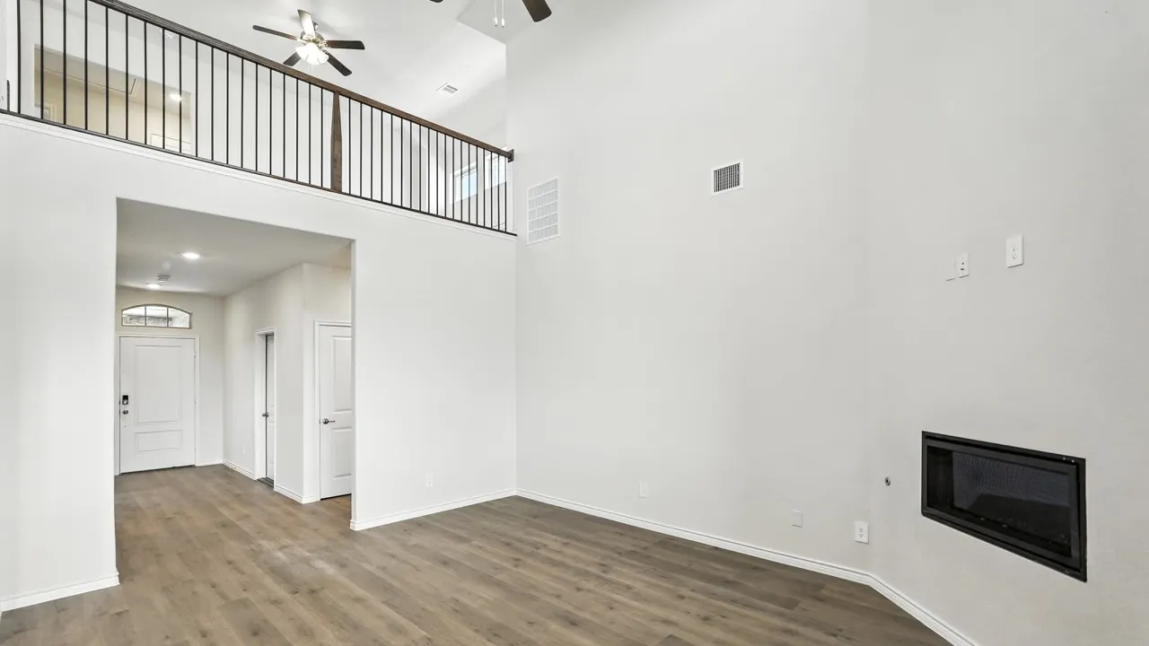 Vaulted ceiling living space featuring wood-finish flooring, a contemporary fireplace, and an upper-level balcony with wrought iron railing