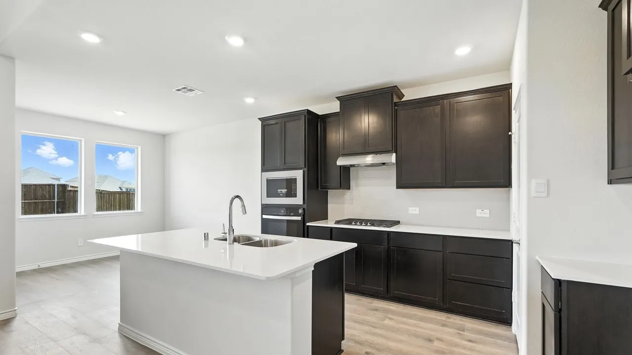 Modern kitchen featuring dark wood cabinetry, light countertops, and a central island with an integrated sink
