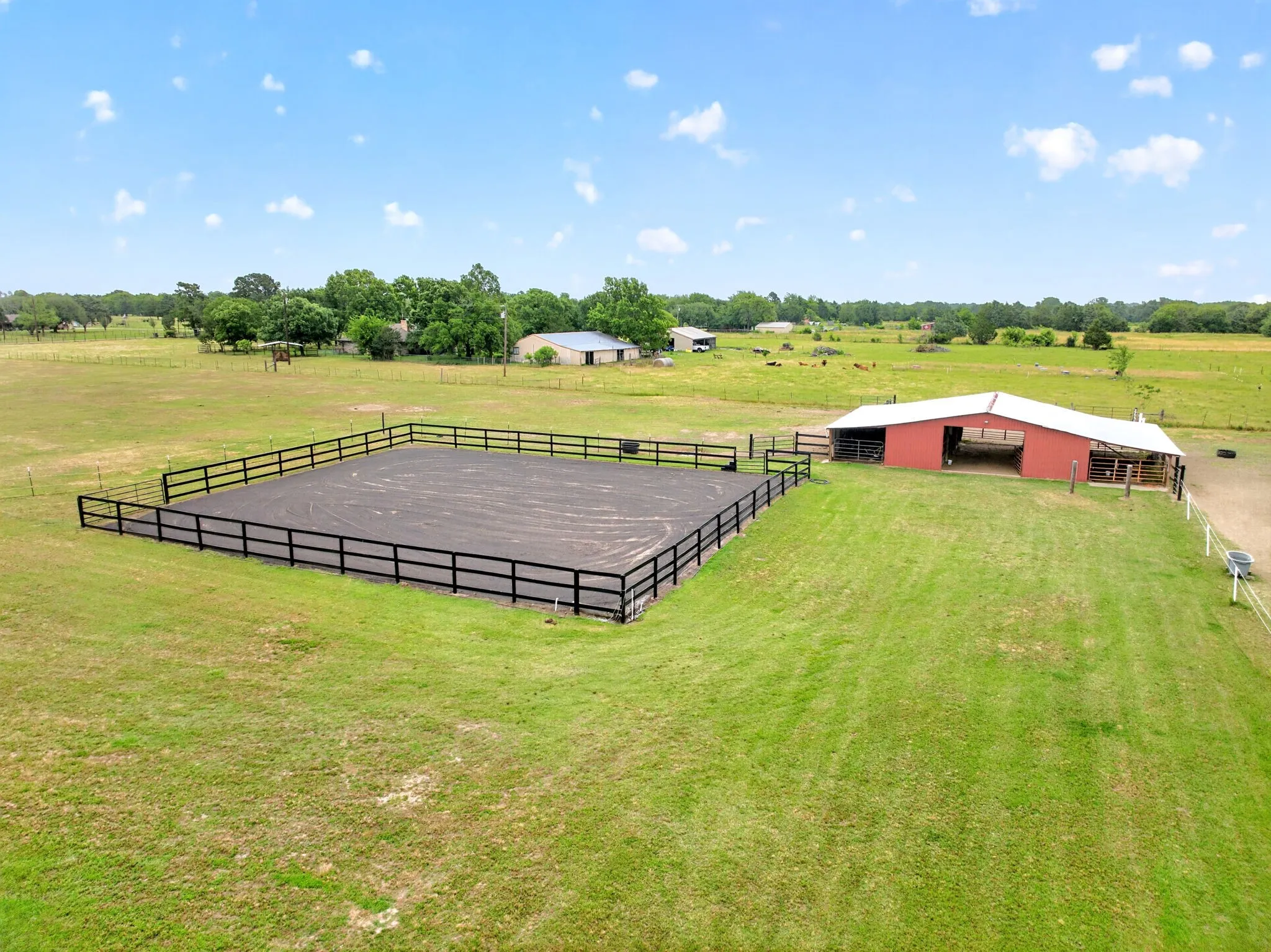 Expansive property featuring a brick residence, detached red barn with covered parking, lush green lawn, mature trees, and perimeter fencing