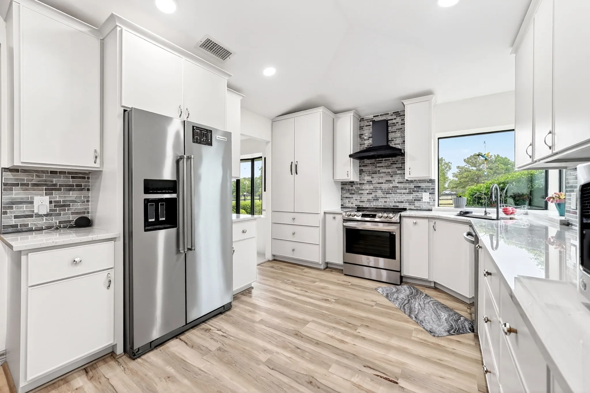 Bright kitchen featuring white cabinetry, stainless steel appliances, light wood-finish flooring, and a mosaic tile backsplash