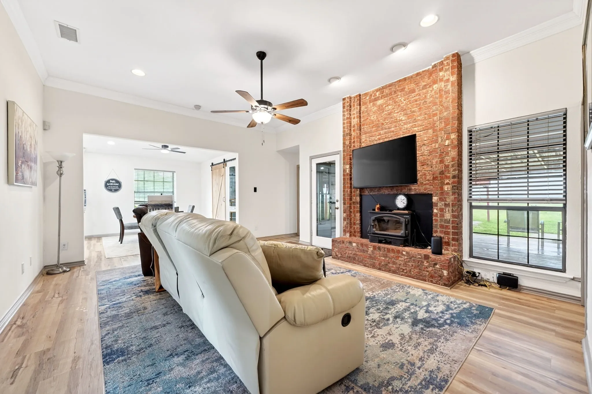 Living area featuring a brick fireplace with a black wood-burning stove, wood-finish flooring, and a ceiling fan