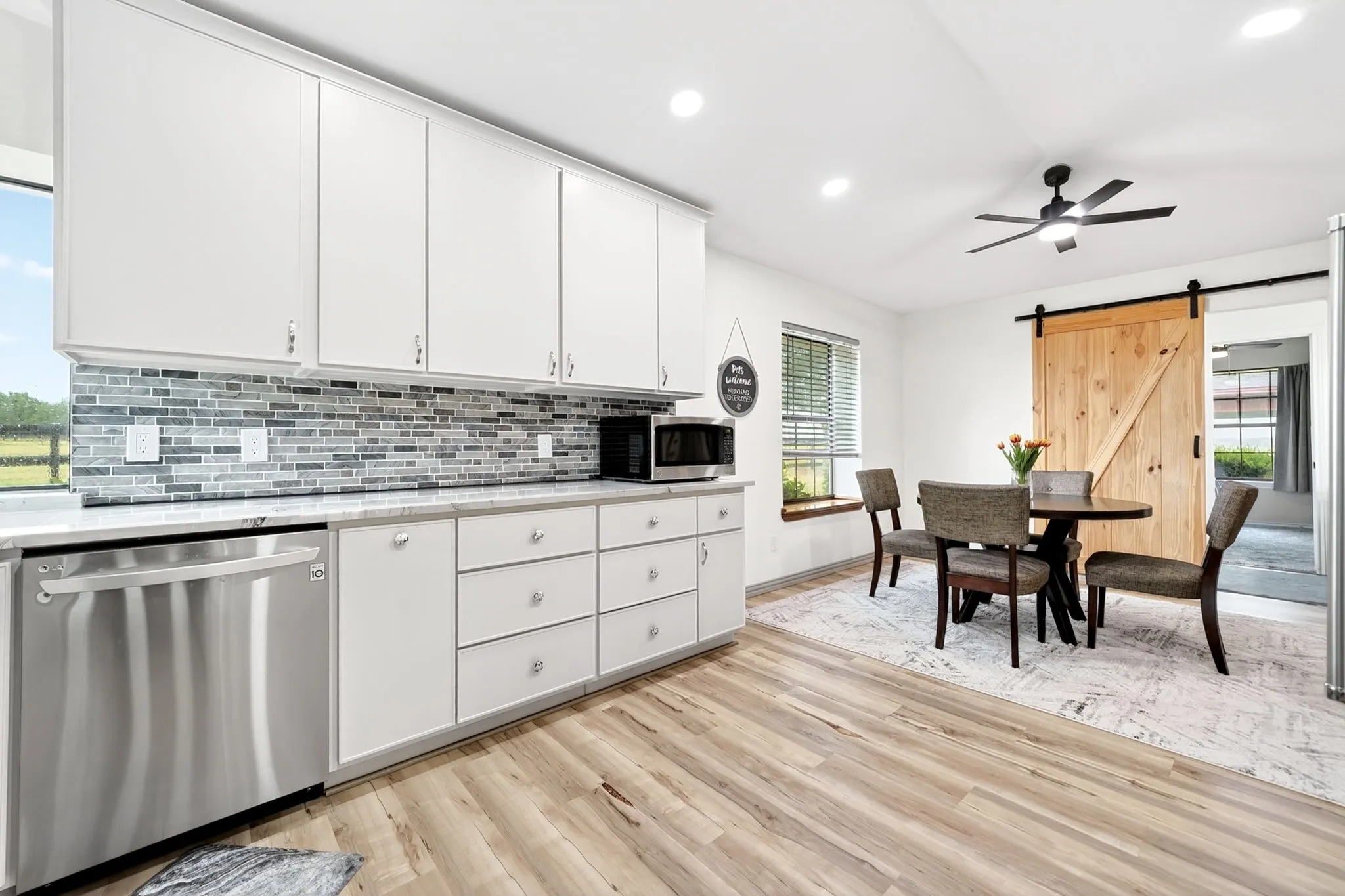 Modern kitchen featuring white cabinetry, a mosaic tile backsplash, stainless steel dishwasher, and wood-finish flooring