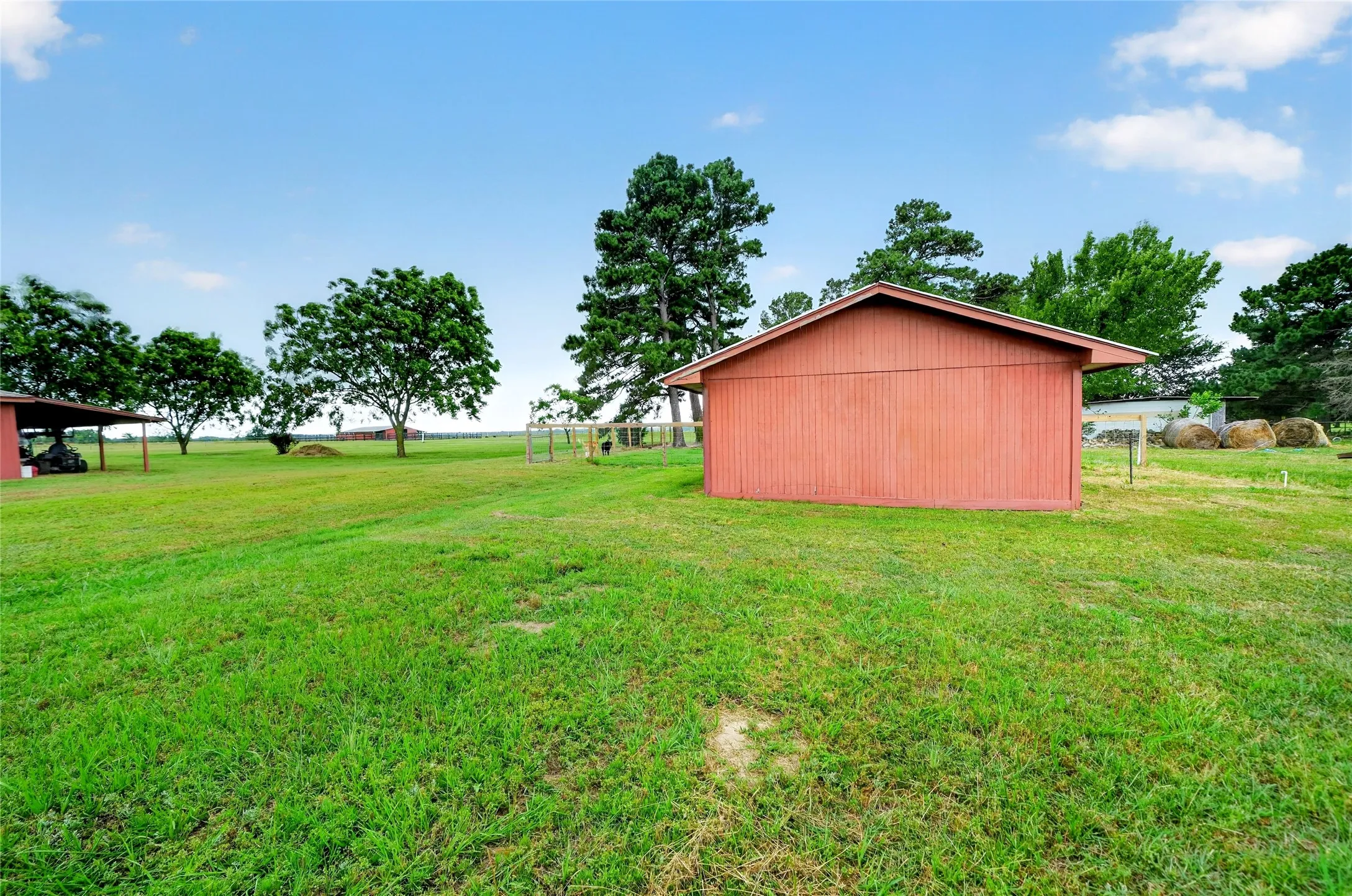 Expansive green grounds featuring a red-sided outbuilding, mature trees, and a covered shed structure