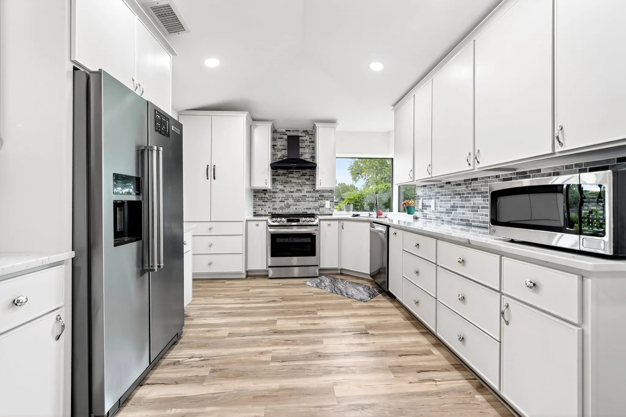 Contemporary kitchen featuring wood-finish flooring, white cabinetry, stainless steel appliances, and a tiled backsplash
