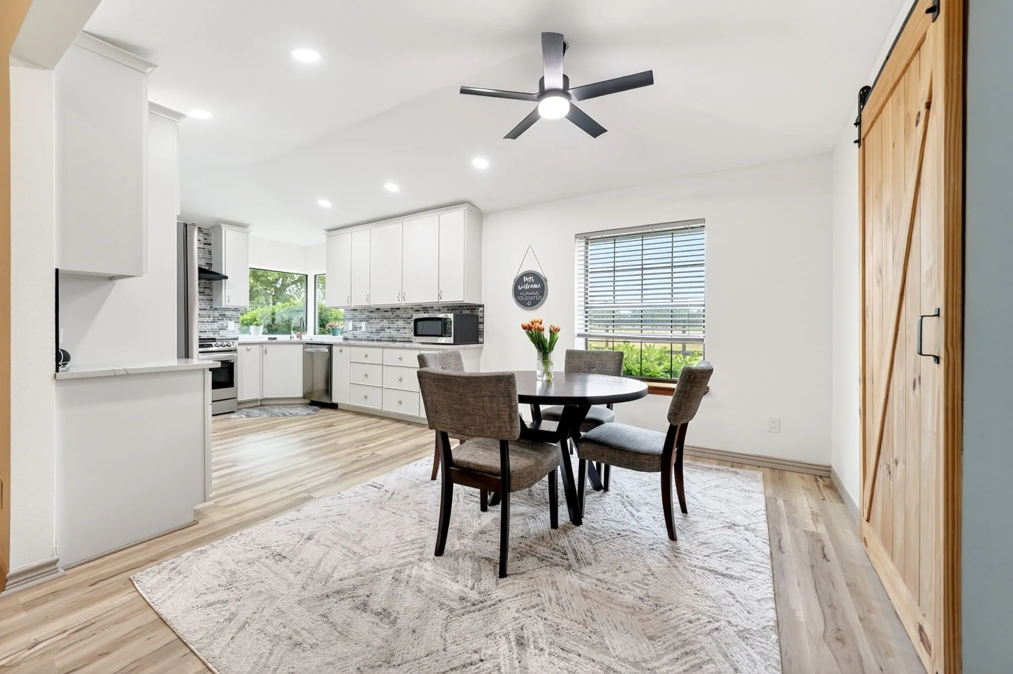 Open concept kitchen and dining area featuring vaulted ceilings, recessed lighting, wood-finish flooring, a contemporary ceiling fan, and a light wood barn door