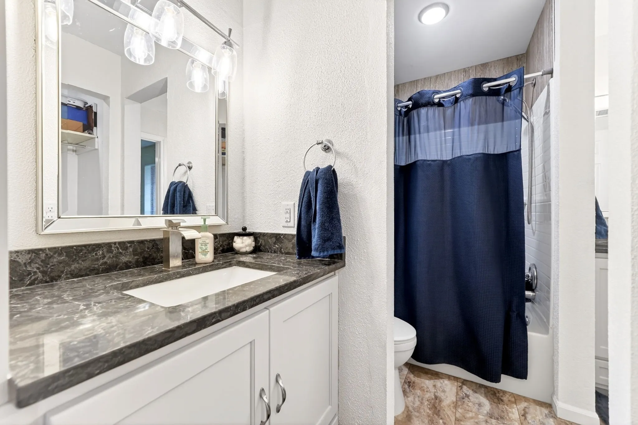 Bathroom featuring a white vanity with paneled cabinetry, a dark marbled countertop, and an undermount sink