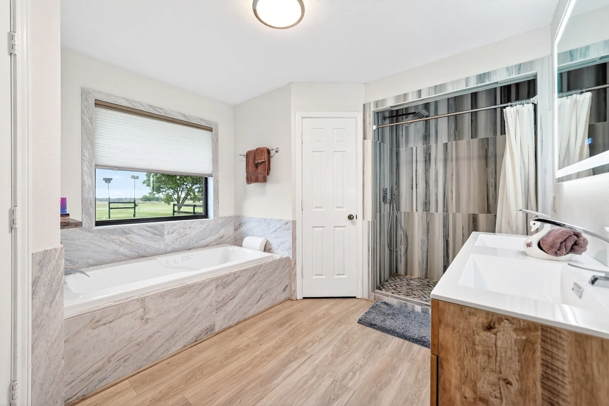 Bathroom featuring a built-in soaking tub, a walk-in shower with glass enclosure, a single vanity with an integrated sink, wood-finish flooring, and a window with horizontal blinds