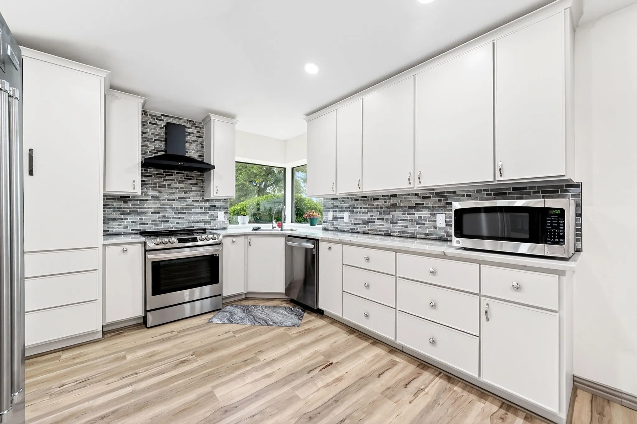Contemporary kitchen featuring white cabinetry, stainless steel appliances, a mosaic tile backsplash, and light wood-finish flooring