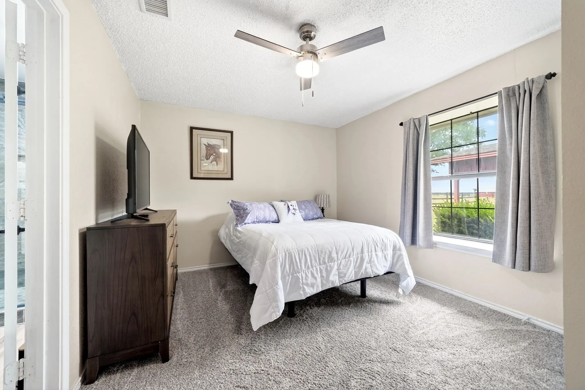 Carpeted room with a ceiling fan light fixture, a window providing natural light, and a white baseboard