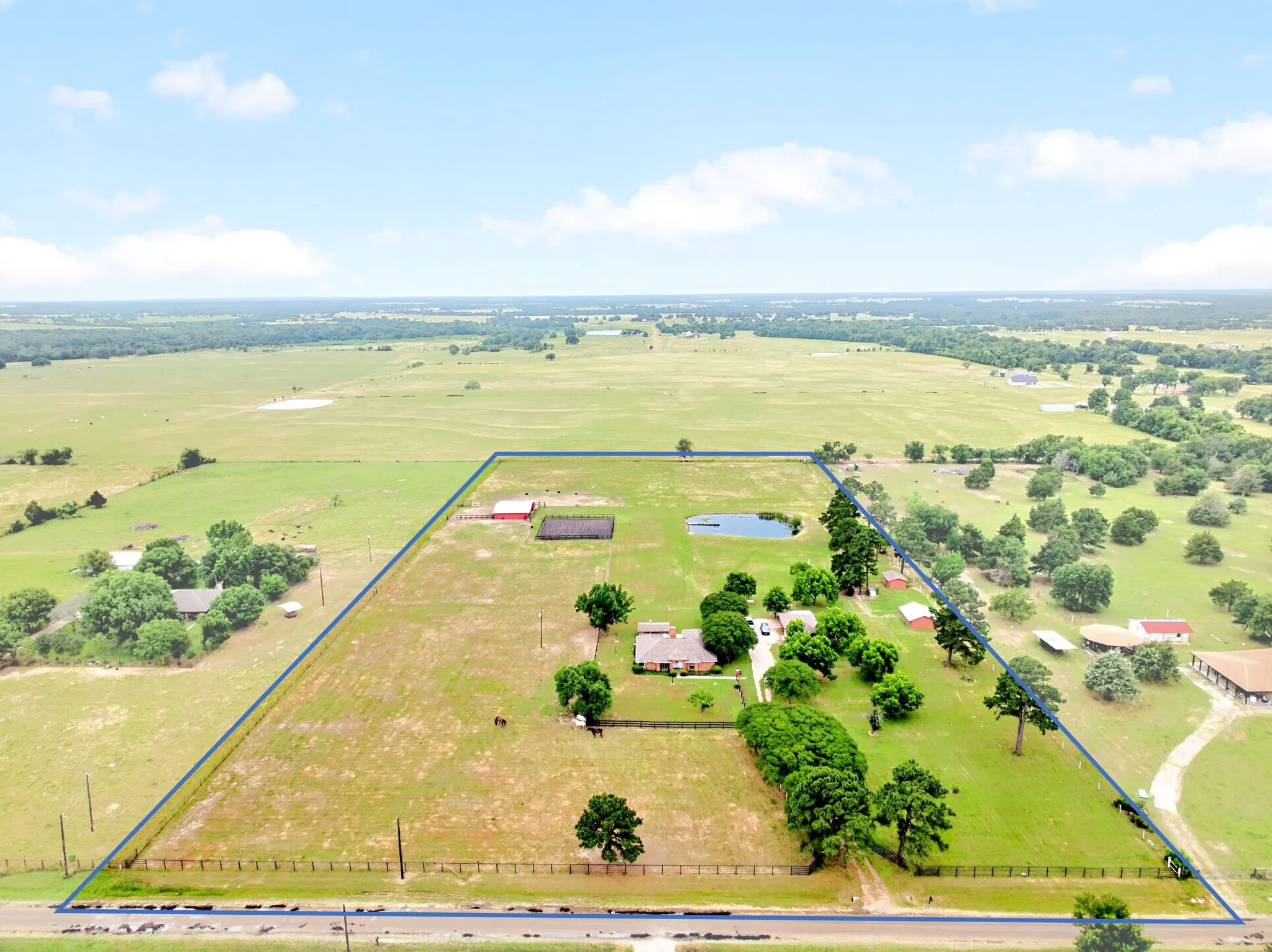 Expansive rural property featuring a primary residence, multiple outbuildings, a private pond, mature trees, and open pastures