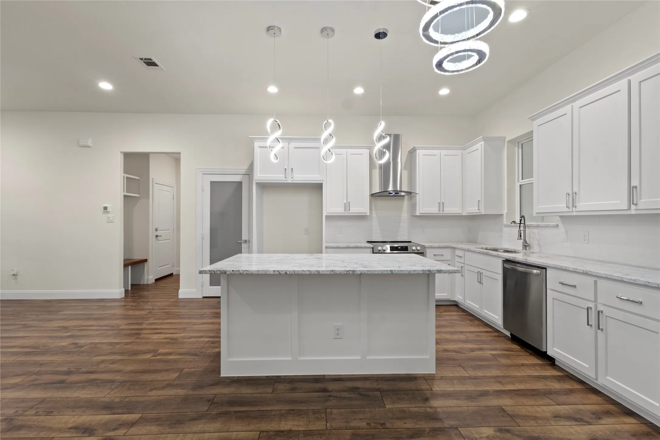 Contemporary kitchen featuring a large central island with a light-toned countertop, white cabinetry, stainless steel appliances, and wood-finish flooring