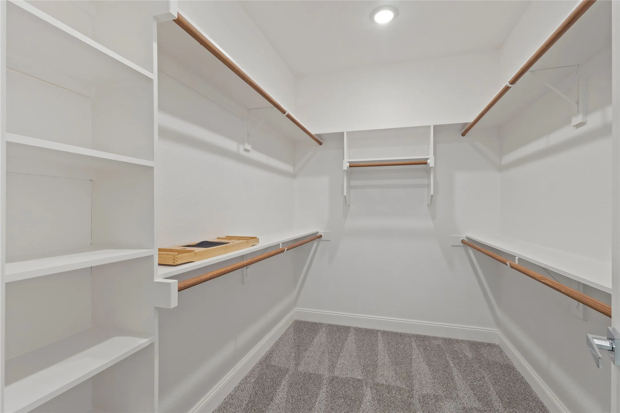 Walk-in closet featuring built-in shelving, white walls, wood-finish hanging rods, and recessed lighting