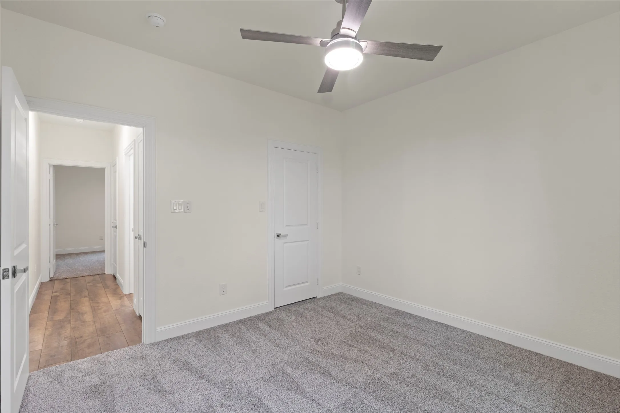 Neutral-toned interior room featuring light gray carpeting and a contemporary ceiling fan with integrated lighting
