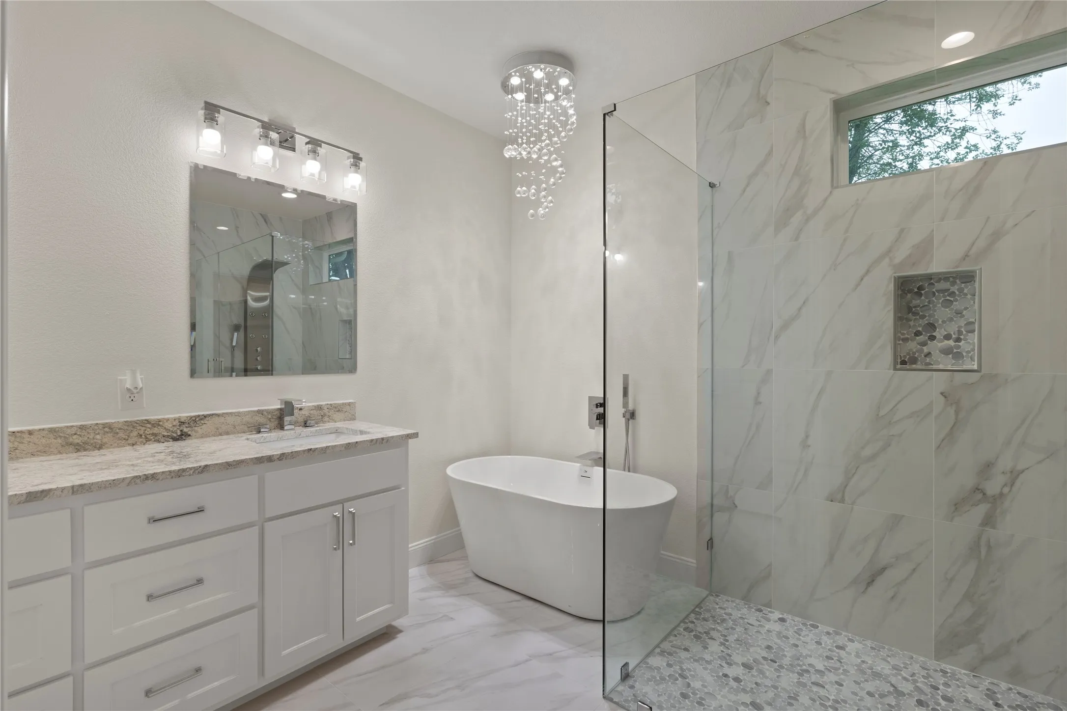 Contemporary bathroom featuring a freestanding tub, glass-enclosed shower with pebble-finish flooring, and a vanity with a stone countertop